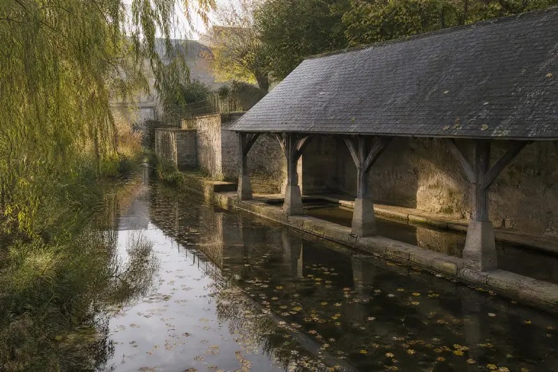 The old covered wash house, with its timber frame and slate roof, reflected in the still river.